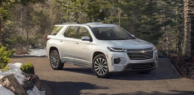New silver 2022 Chevrolet Traverse parked in a nature park surrounded by light snow. The road is clear. 