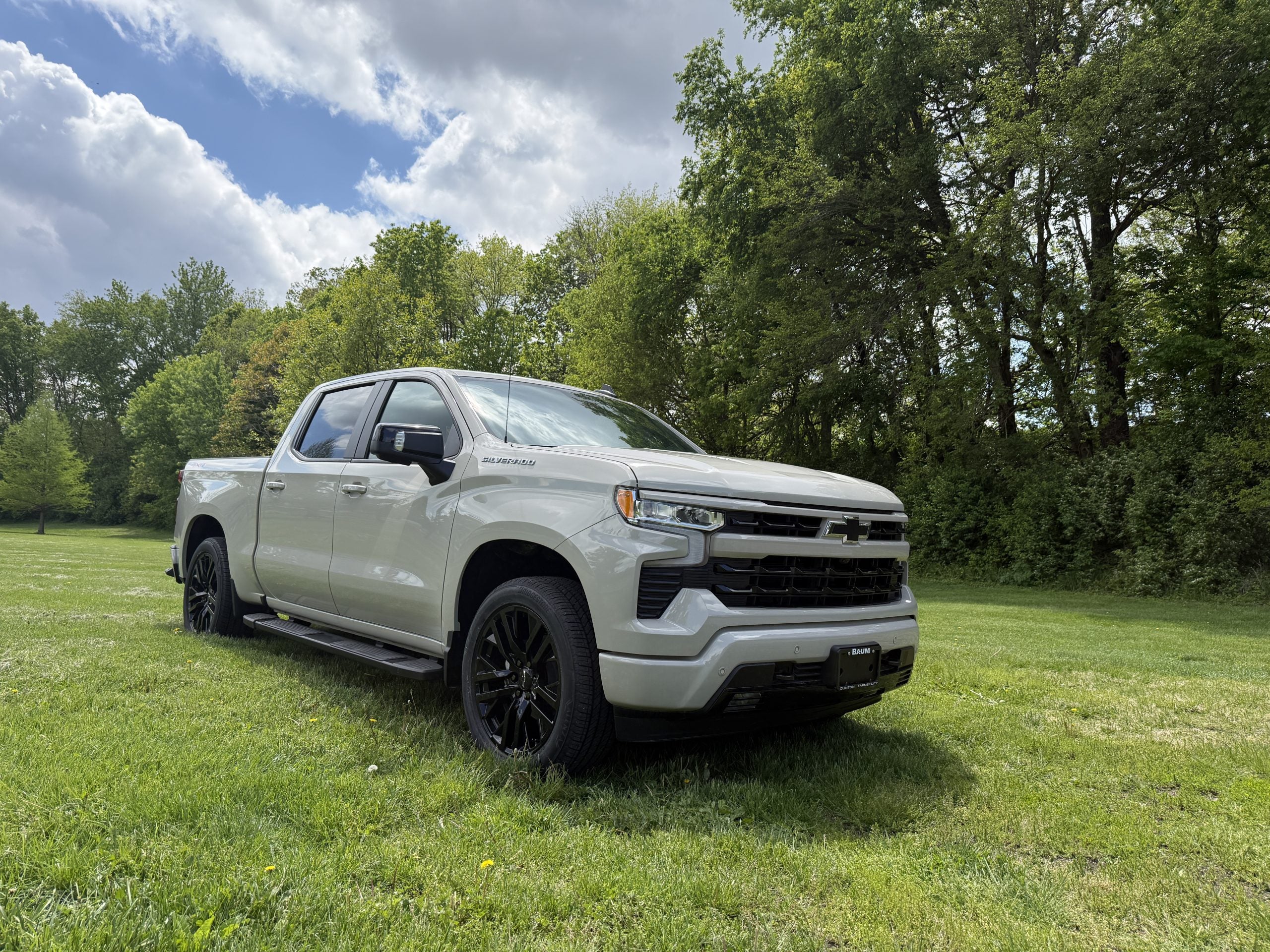 2026 Chevrolet Silverado near Clinton IL, shown in country outdoor setting with green grass and trees behind.