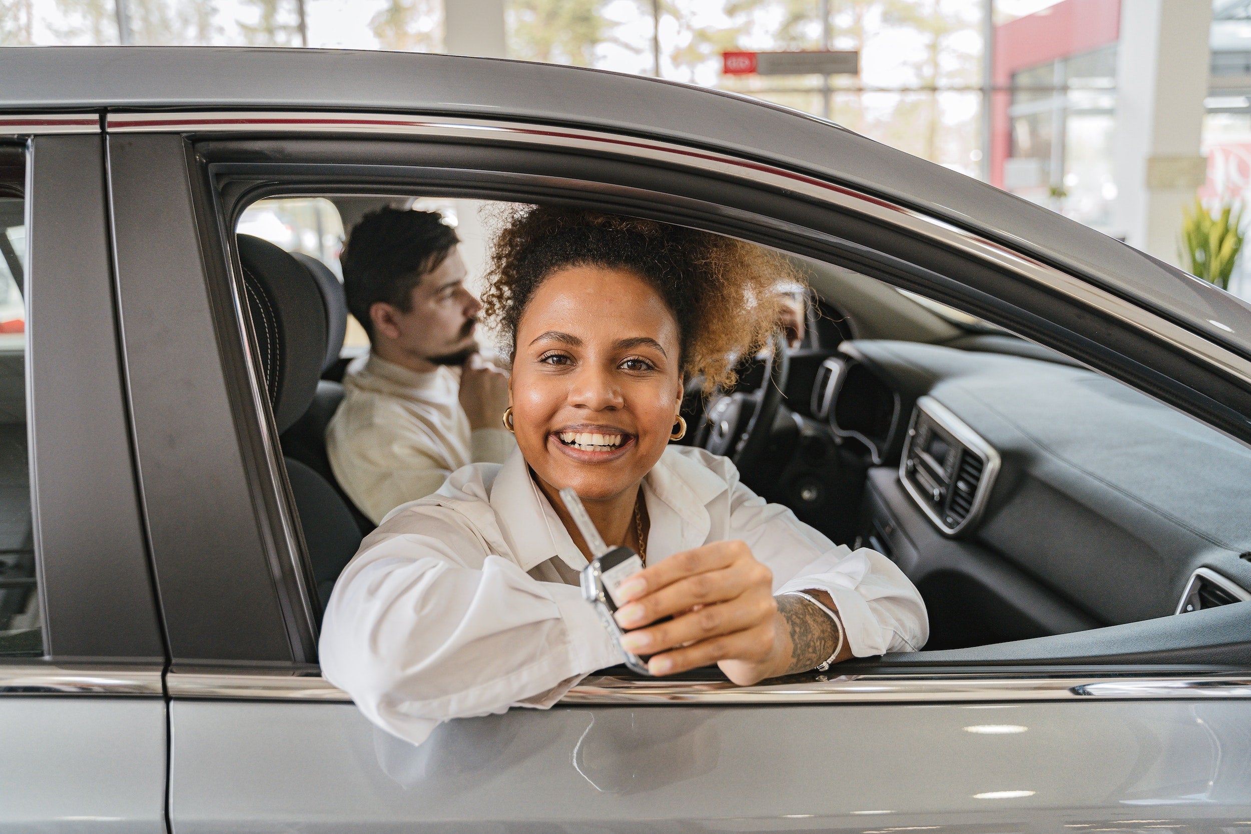 Woman leaning out of a car window showing off a key to a car.