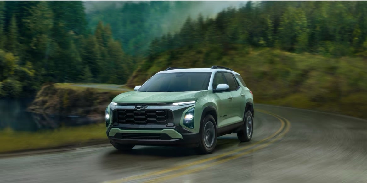 A green 2025 Chevy Equinox driving on road in rain.