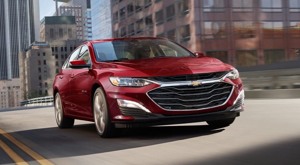 Red 2024 Chevy Malibu driving on a city street.