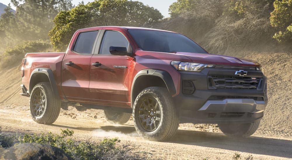 A red 2023 Chevy Colorado Trail Boss is shown on a dusty trail after leaving a Chevy dealer in Olive Branch, MS.