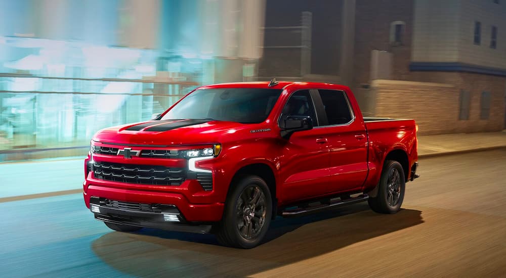 A red 2024 Chevy Silverado 1500 RST is shown driving to a Chevy dealer near Iuka.