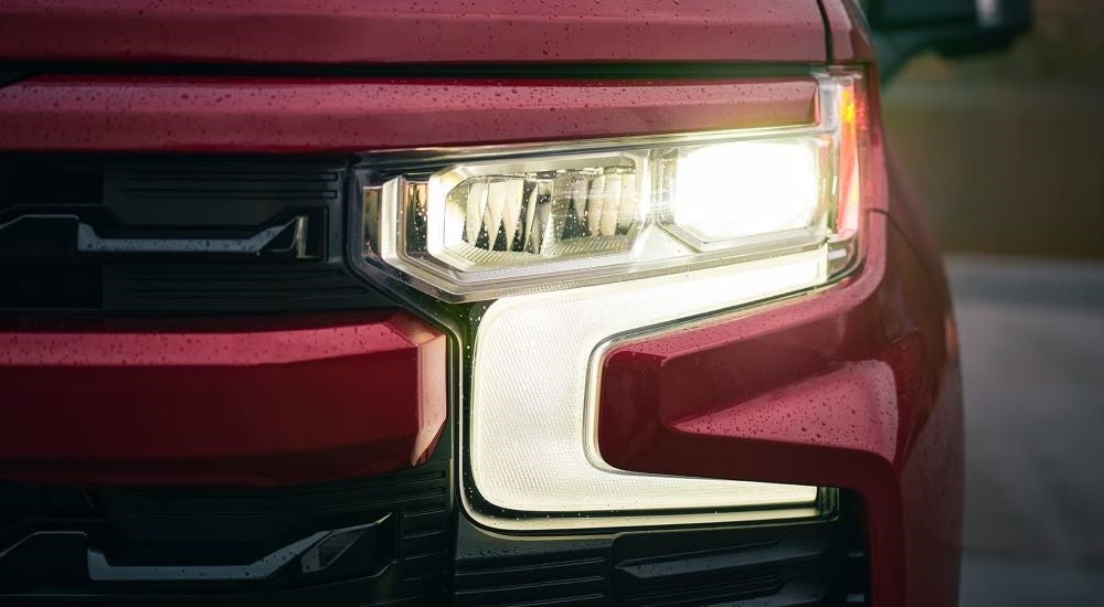 A close-up shows the illuminated driver side headlight on a red 2023 Chevy Silverado 1500.