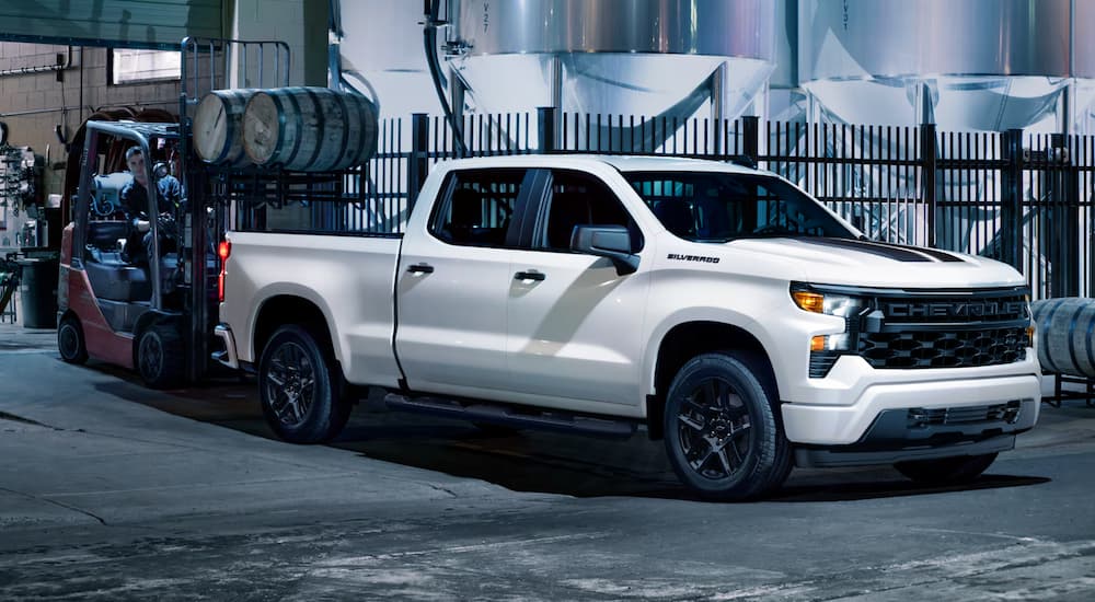 A white 2025 Chevy Silverado 1500 Custom Rally Edition is parked next to a forklift.