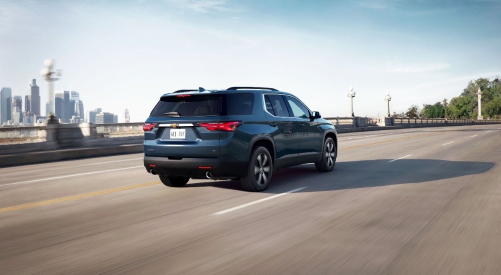 A dark blue 2023 Chevy Traverse is shown driving near a city after leaving a Chevy Traverse dealer.