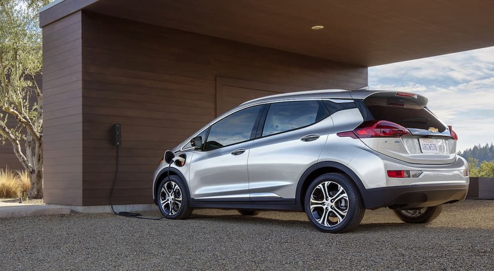 A silver 2020 Chevy Bolt charging outside of a modern home.