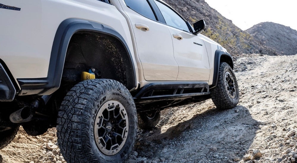 A tan 2023 Chevy Colorado ZR2 is shown driving on a rocky trail after leaving a Chevy dealer in Collierville, TN.