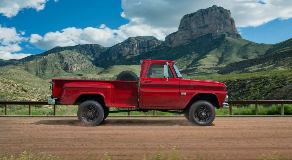 A red first-generation Chevy C/K pickup truck driving on a country road.