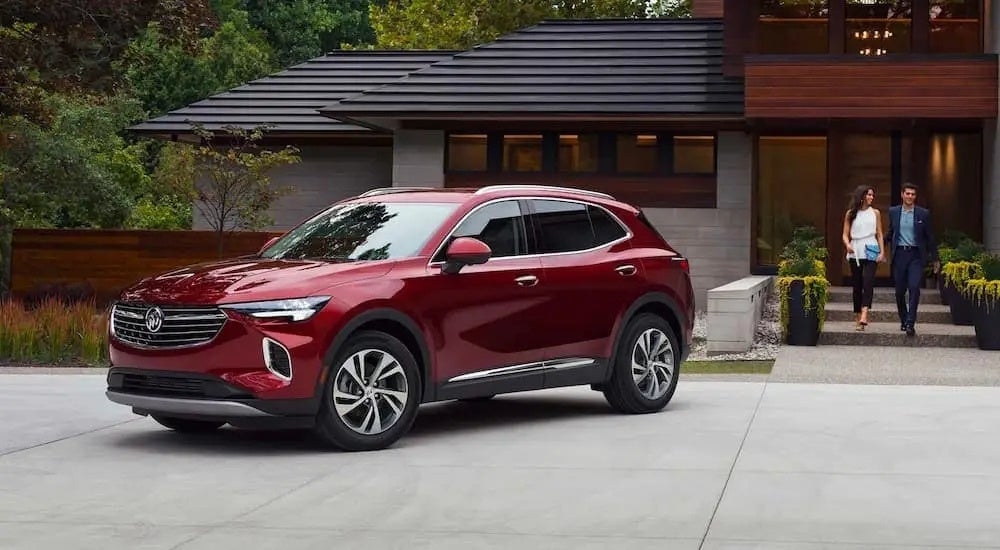 A couple walks out of their modern home towards a red 2021 Buick Envision parked in their driveway.