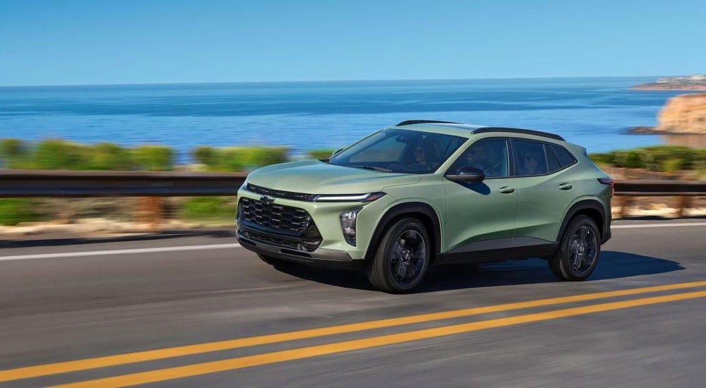 A green 2025 Chevy Trax ACTIV is shown driving on a highway near an ocean.