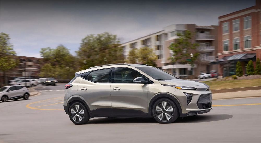 A tan 2022 Chevy Bolt EUV driving on a city street with brick buildings after looking at Chevy SUVs.
