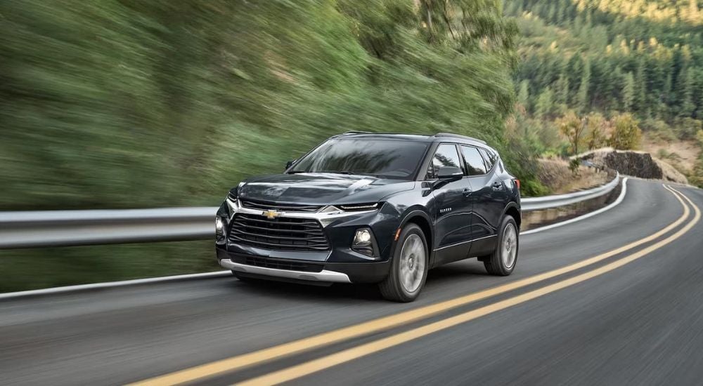 A black 2021 Chevy Blazer is shown driving on a tree-lined road.