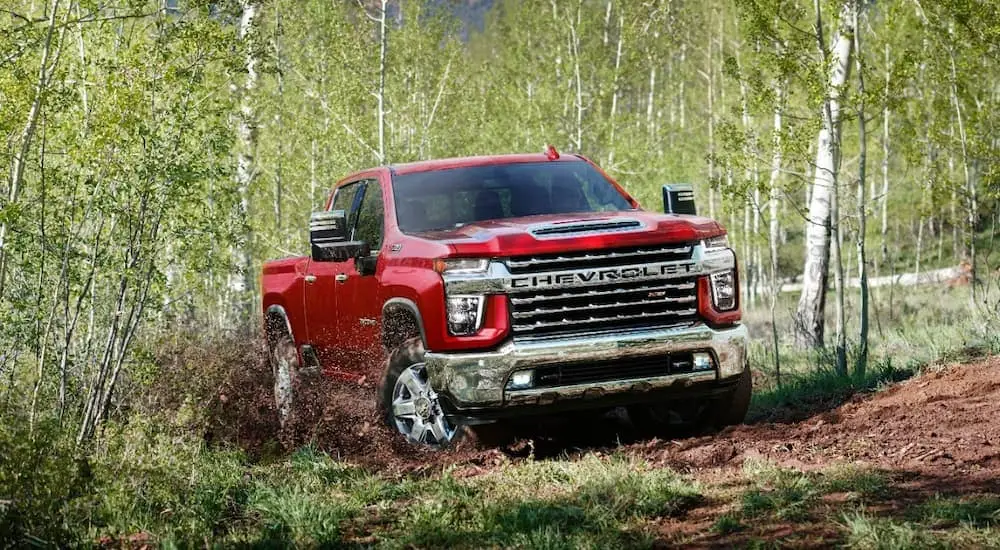 A red 2022 Chevy Silverado 2500 HD is off-roading on a dirt trail in the woods.
