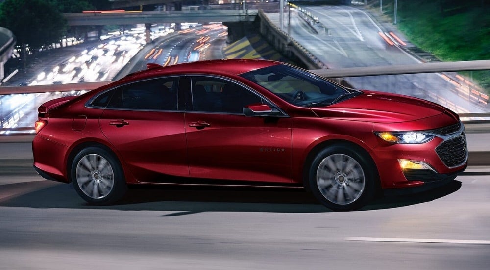 A red 2023 Chevy Malibu is shown driving on a bridge.