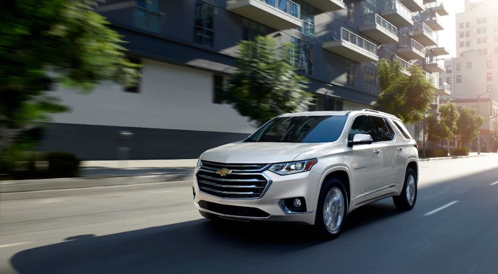 A white 2020 Chevy Traverse High Country driving on a city street with trees.