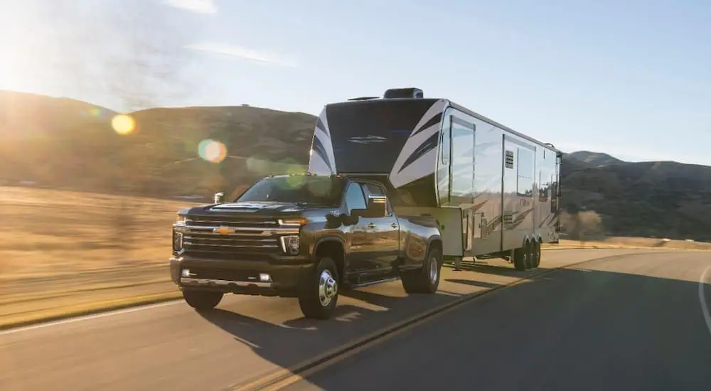 A black 2020 Chevy Silverado 3500HD, a popular used Chevy truck for sale, is towing a large camper trailer.