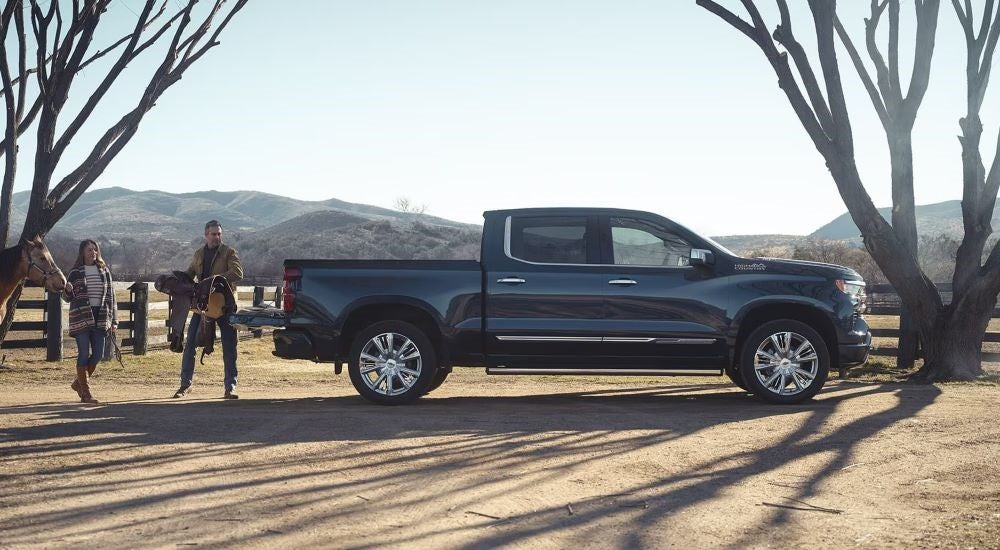 A black 2024 Chevy Silverado 1500 High Country is shown parked near a tree.