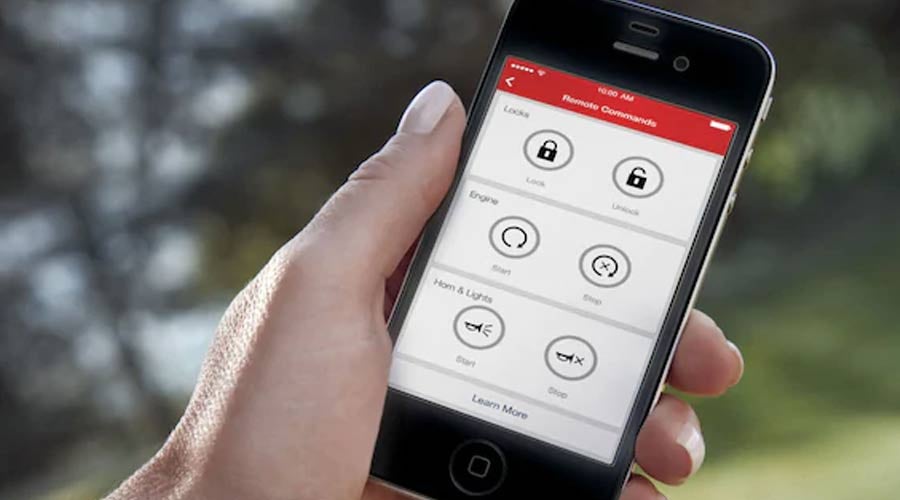 Hand holding a cell phone with the My Chevrolet Rewards app / My GM Rewards app displayed, including buttons for remote start and vehicle locks