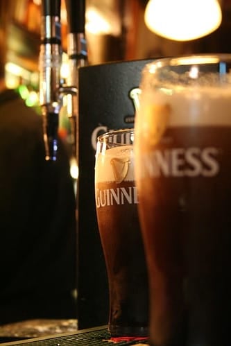 Two full Guinness pints on bar with bar tap in background