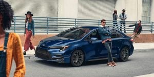 A blue Toyota sedan parked on an urban street and surrounded by fashionable drivers.