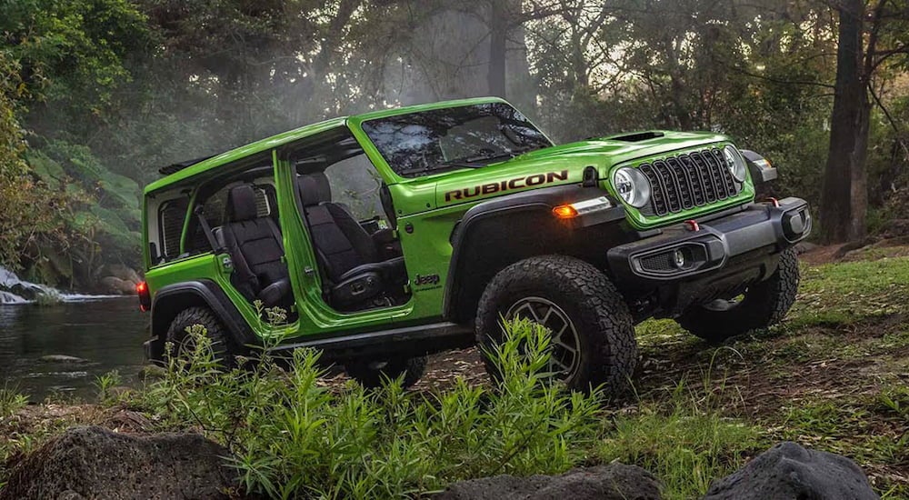 Green 2026 Jeep Wrangler driving off-road through a forest.