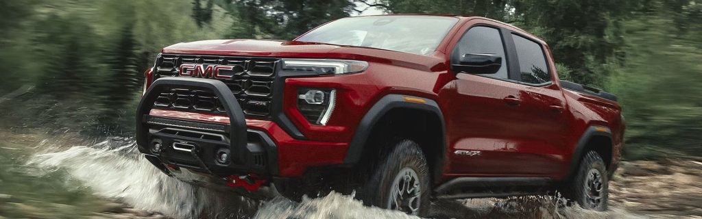 Red GMC pickup truck splashing through water on a forest trail