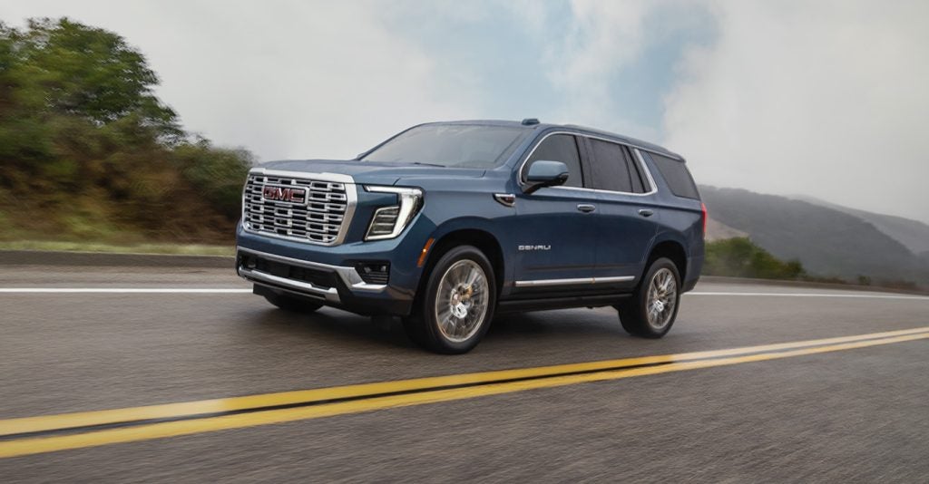 A blue GMC Yukon Denali driving along a scenic highway.