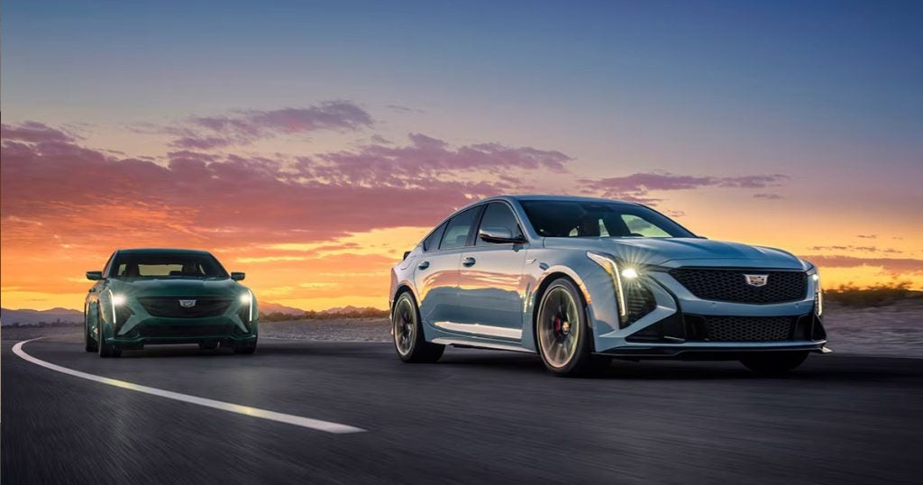 Two Cadillac CT5 models driving along an empty road with the sunrise behind them.