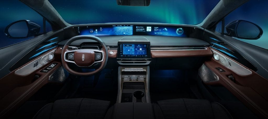 A futuristic luxury car interior with panoramic digital displays and ambient lighting set against a night sky.
