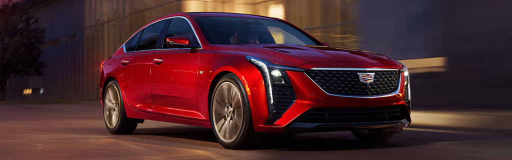 A metallic red Cadillac sedan driving at speed on a city street.
