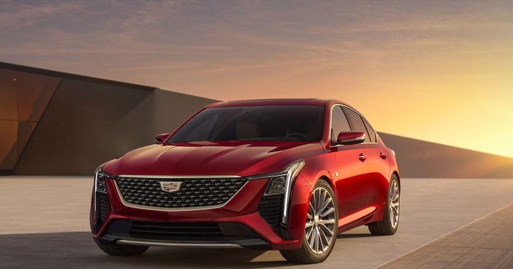 Red 2025 Cadillac CT5 sitting next to a modern building with the sunset behind it.