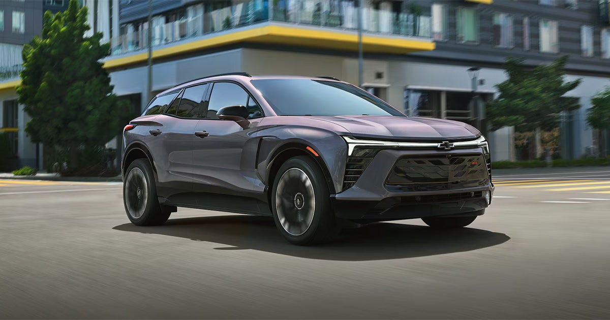 Silver Chevrolet Blazer EV driving on city street with modern buildings in background