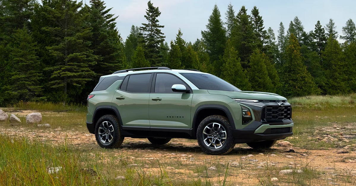 Light green 2026 Chevrolet Equinox Activ with black cladding and off-road tires on dirt terrain with evergreen forest background