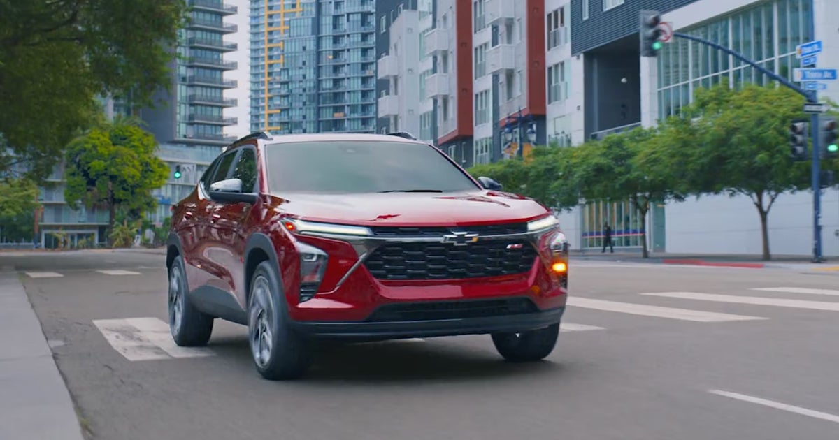 Red Chevrolet Blazer SUV driving on city street with modern buildings in background