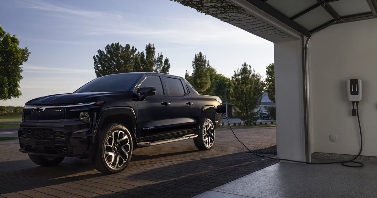 Black Chevrolet Silverado EV pickup truck charging in residential garage with wall-mounted charging unit