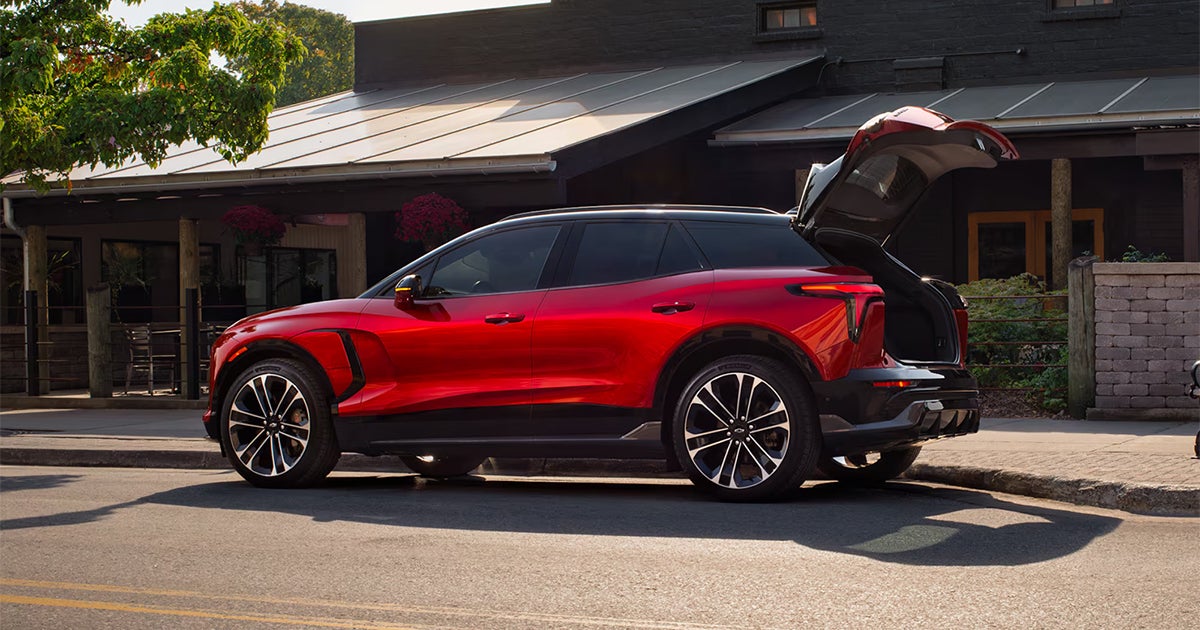 Red Chevrolet Blazer EV with open rear hatch parked in front of modern home with solar panels
