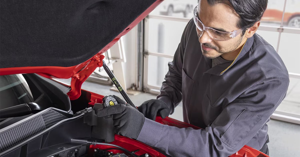 Chevrolet service technician performing maintenance under hood of red vehicle in service bay