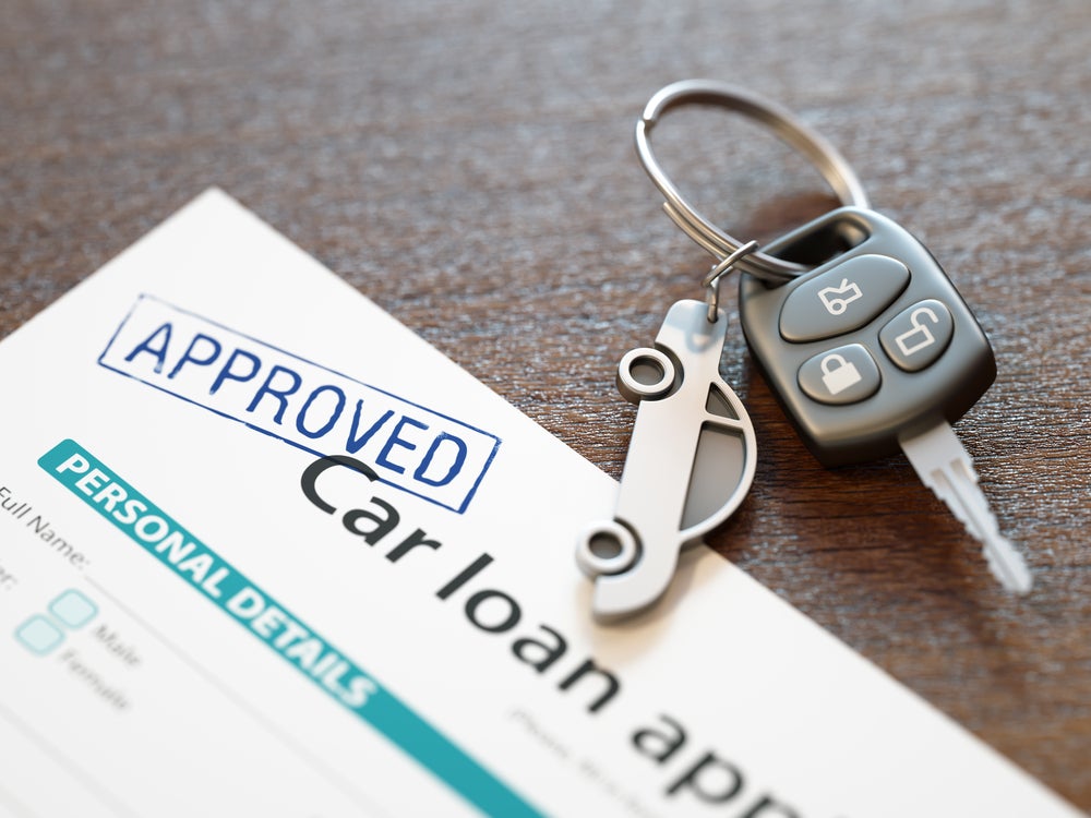 Approved car loan form with car keys on a wooden surface.