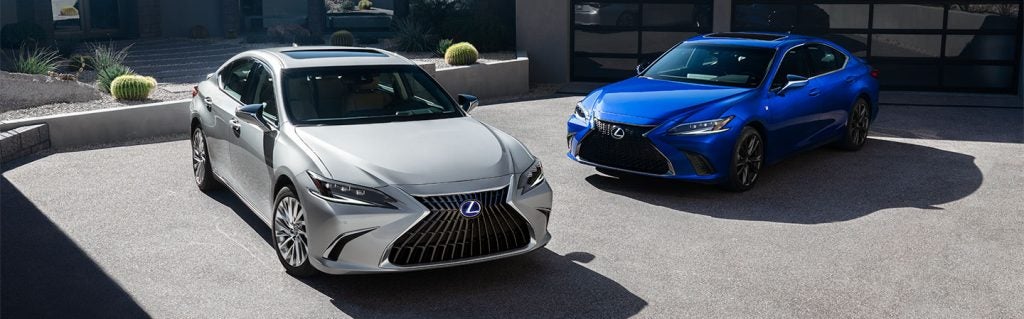 Two Lexus ES sedans, one silver and one blue, parked in a modern driveway with a minimalist design