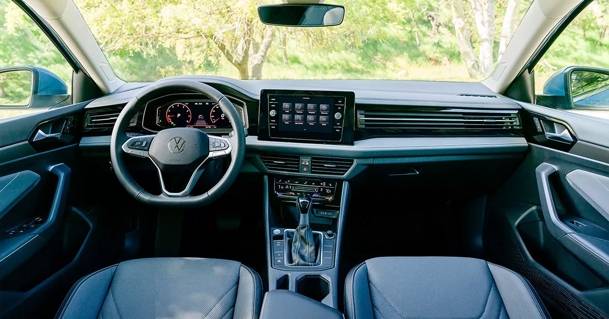 Volkswagen interior dashboard view with digital cockpit, infotainment screen, blue leather seats, trees in background