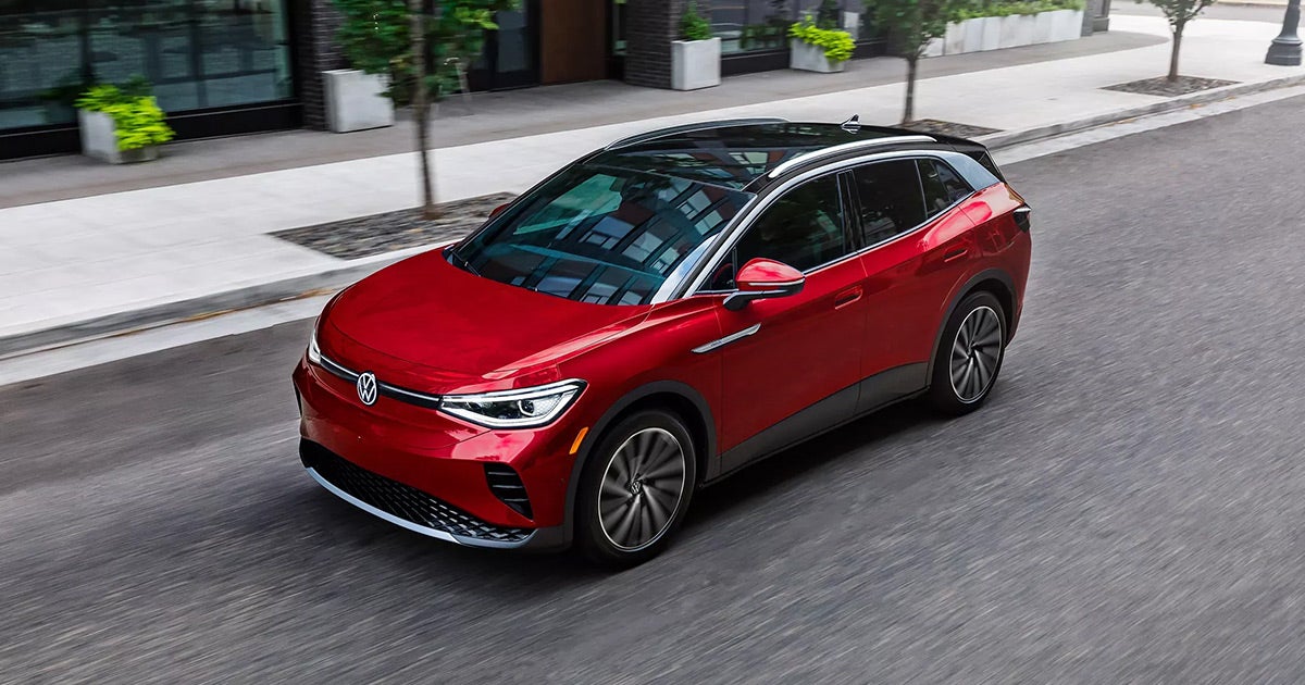 Red Volkswagen ID.4 electric SUV driving on city street, sleek modern design, black roof