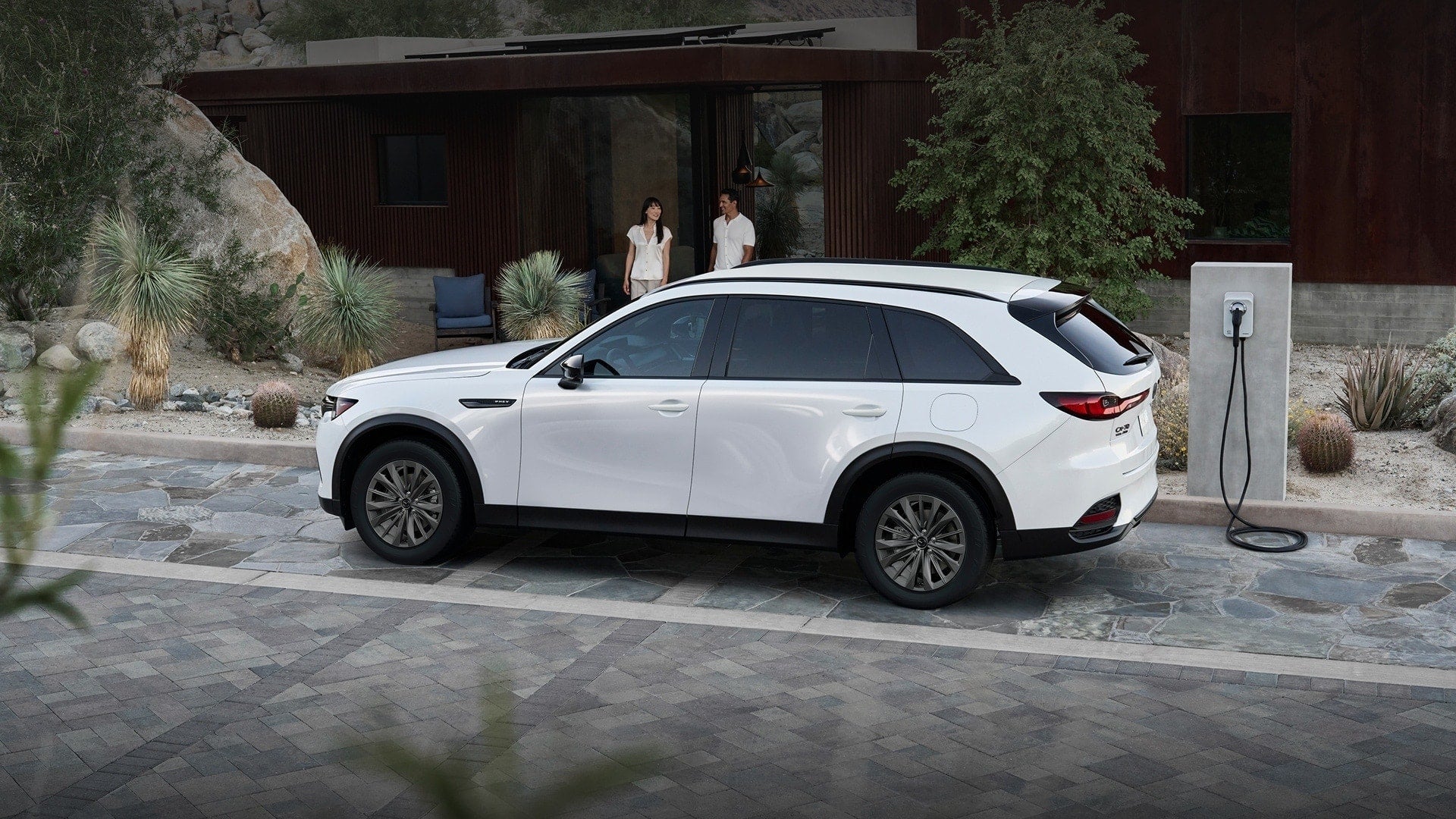 2026 Mazda CX-70 PHEV parked near a charging station with a modern house in the background.