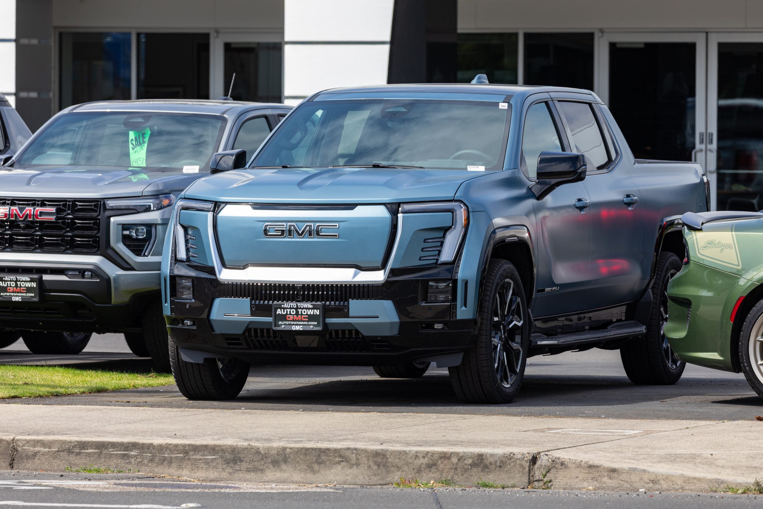 Beaverton, OR, USA - June 15, 2025 - Close-up of a brand new GMC Sierra Denali EV electric pickup truck in matte blue finish, featuring bold front grille design, parked at a GMC dealership lot