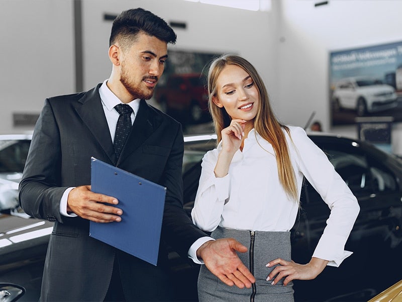 A Sales Professional is showing a woman a vehicle she's interested in in the showroom