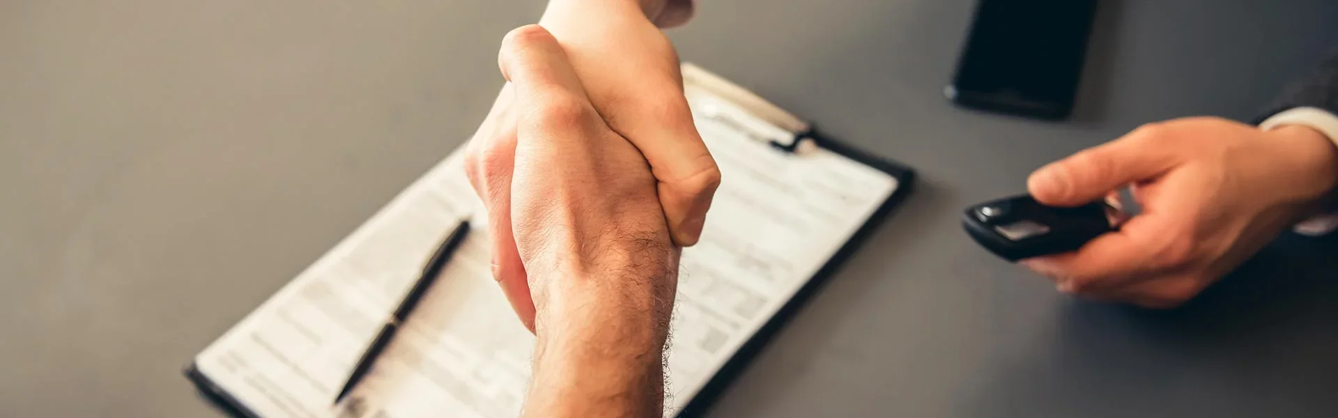 A customer and a salesperson's handshake over the paper agreement for purchasing a vehicle and keys being given to the purchaser.