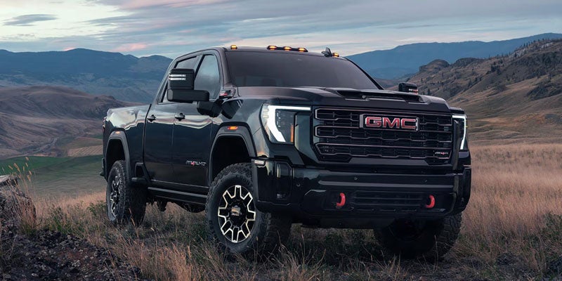 Black GMC Sierra 2500HD pickup truck parked on rugged terrain with mountains in the background.