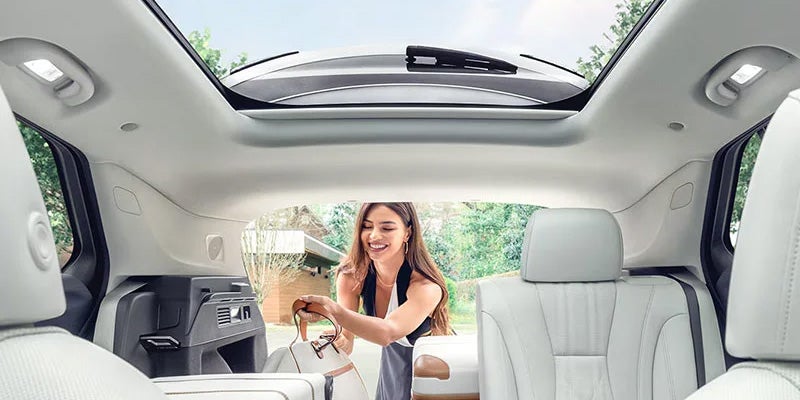 A young woman is placing luggage in the trunk of her white Buick Envision interior with panoramic sunroof as we view her from the front seat