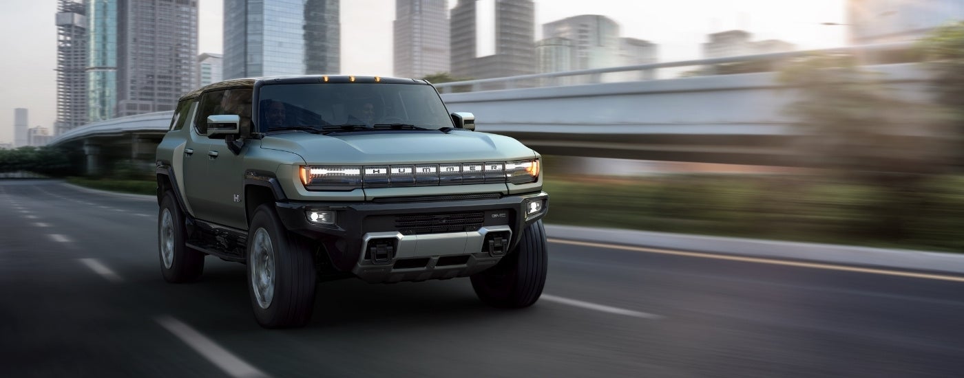 A green 2022 GMC Hummer EV is shown driving past skyscrapers.