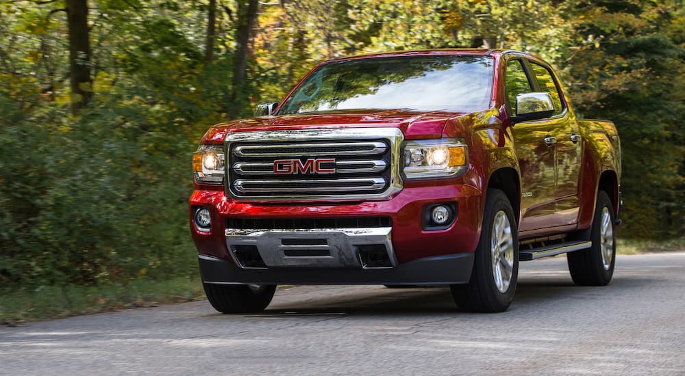 Red 2019 GMC Canyon SLT driving on a tree-lined road